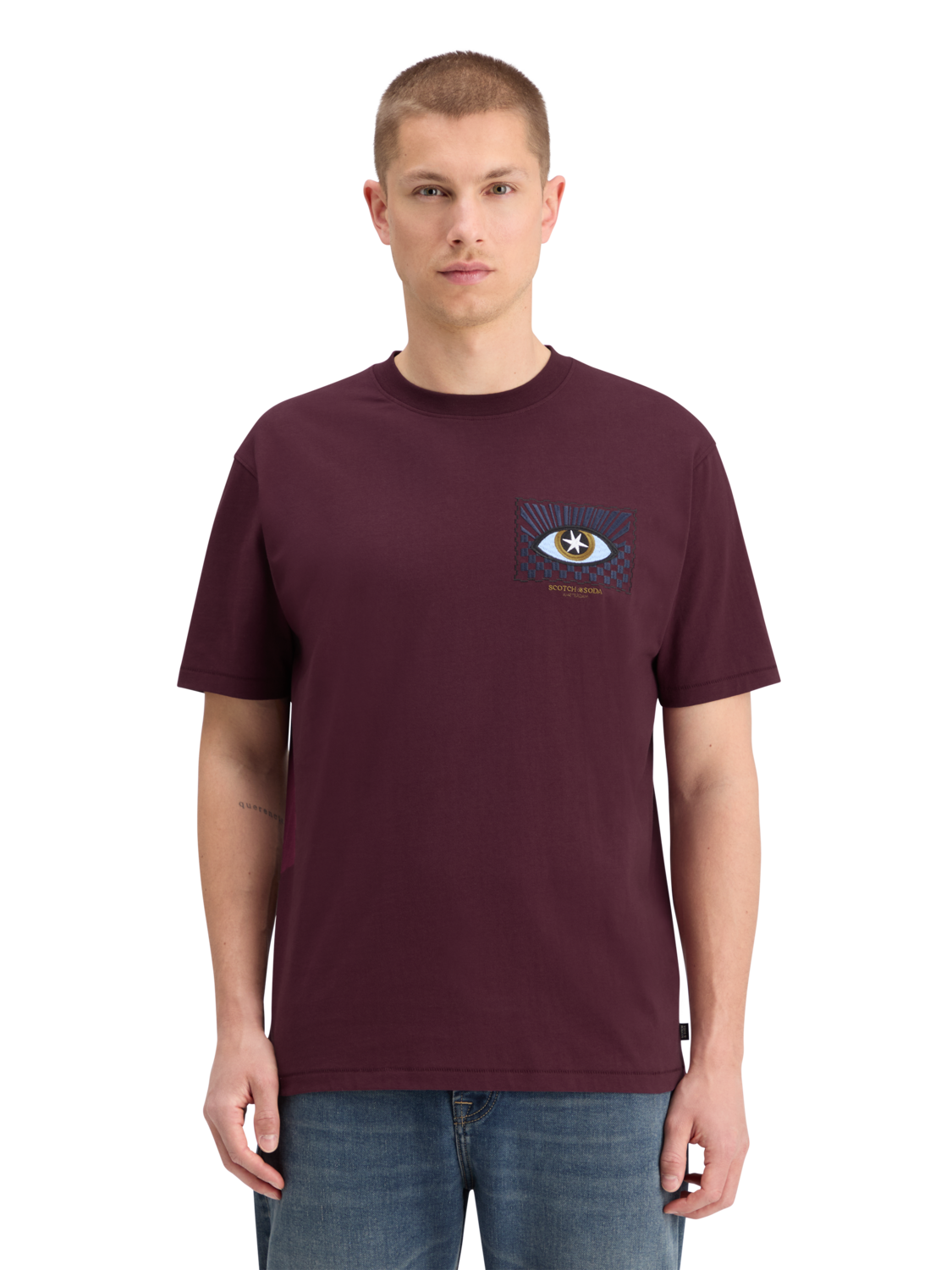 A man wearing a relaxed fit maroon t-shirt with front artwork, standing against a plain background.