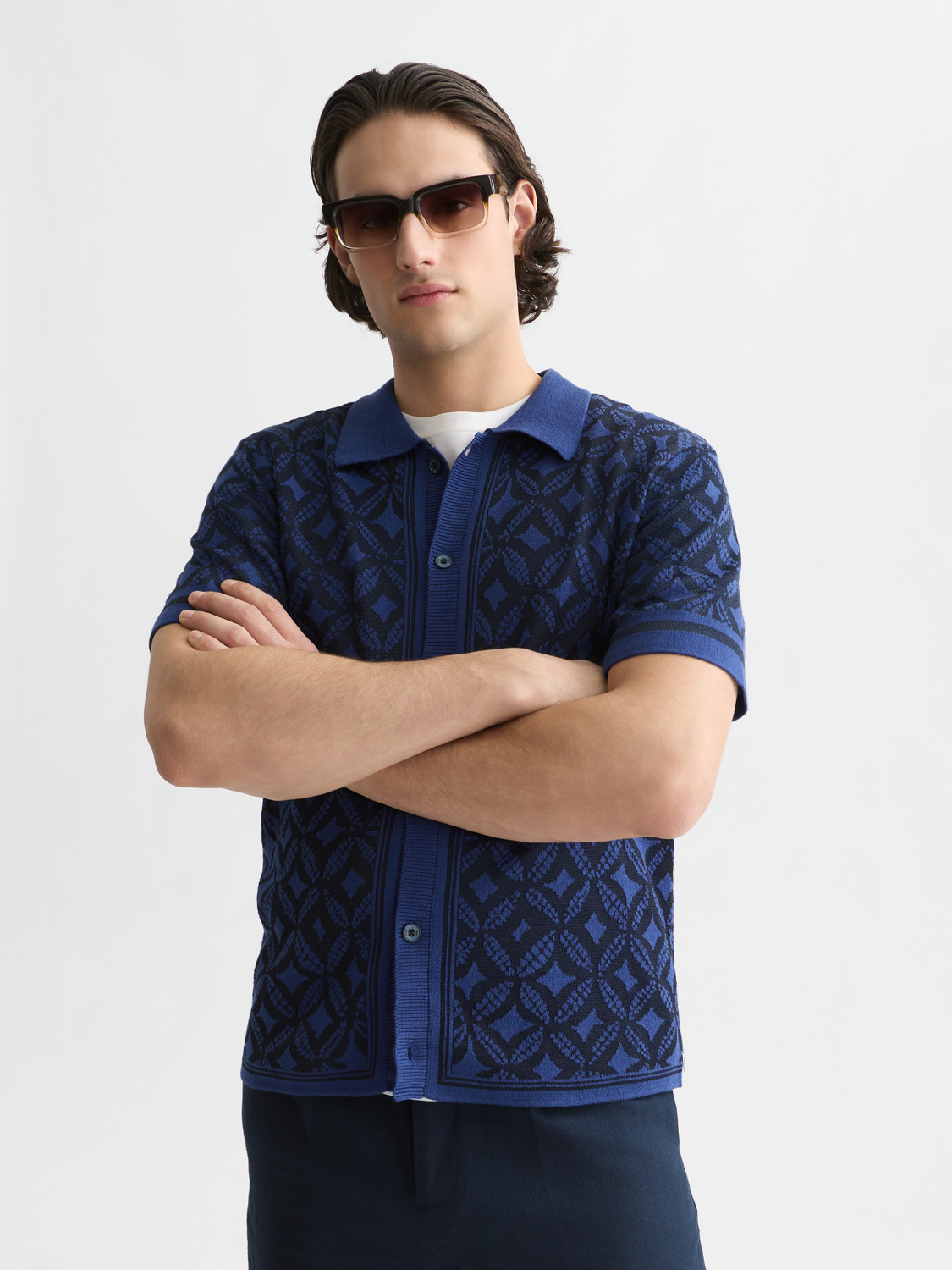 Man wearing a blue patterned shirt with sunglasses on a white background