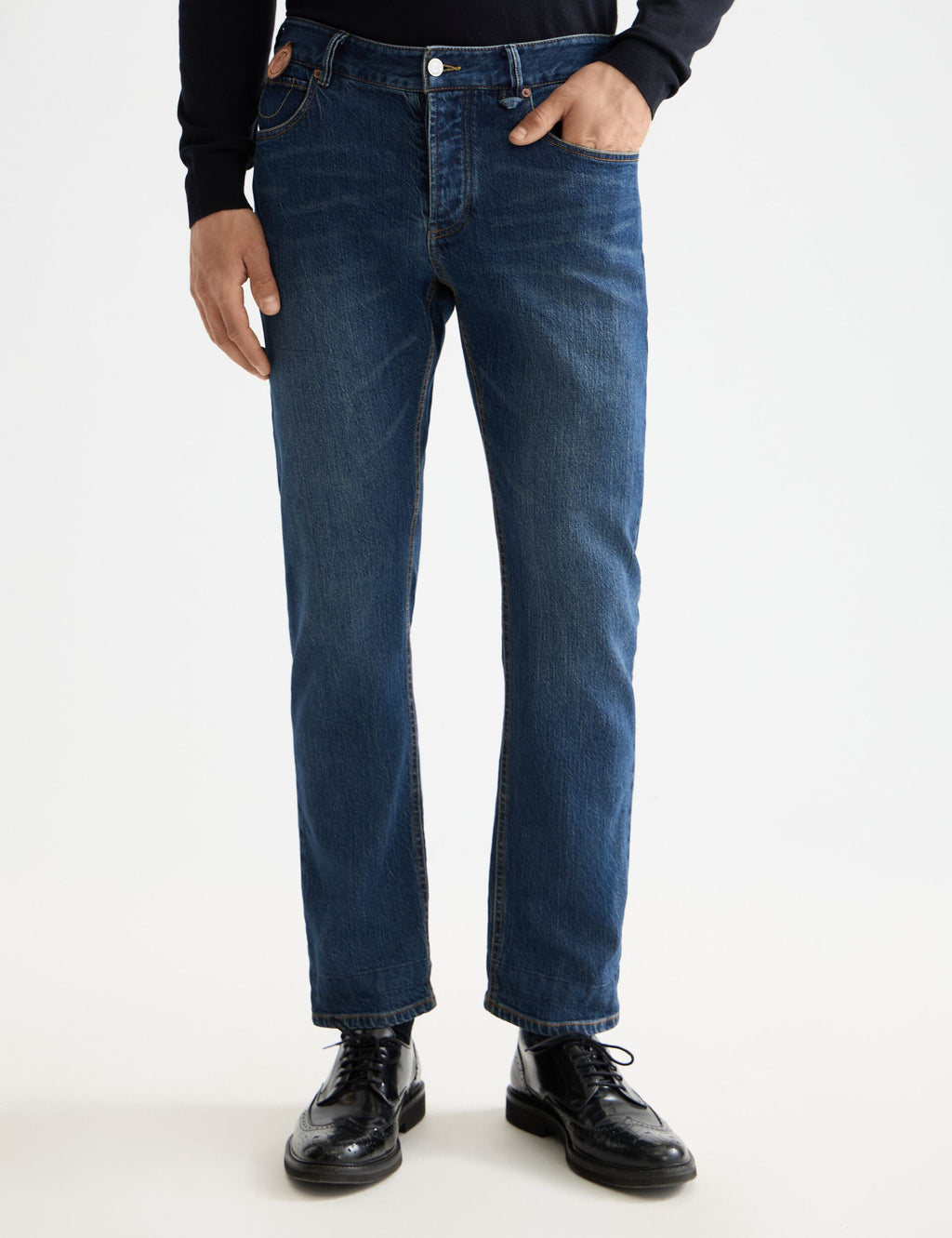 Person wearing blue jeans and black shoes on a white background