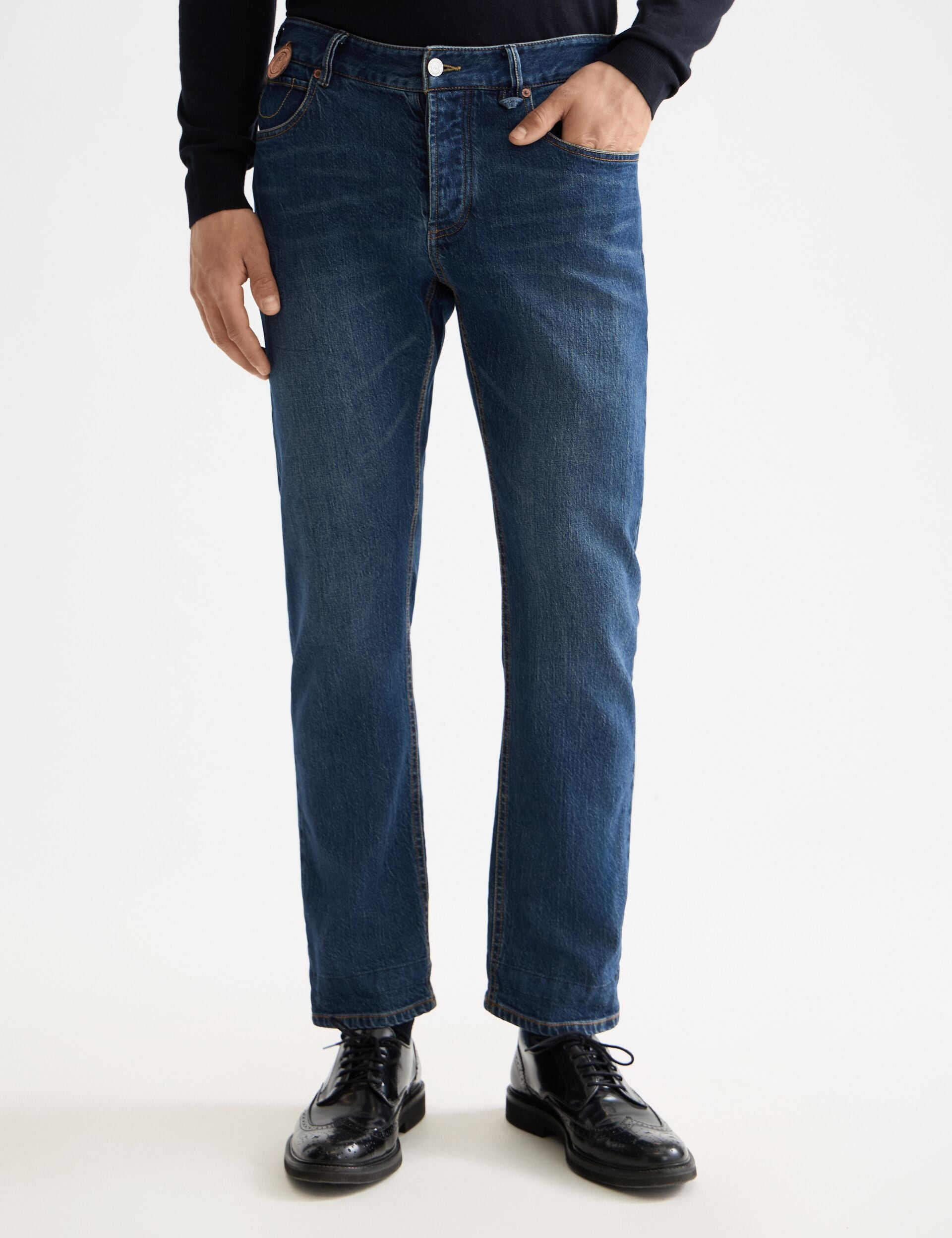 Person wearing blue jeans and black shoes on a white background