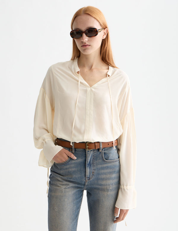 Woman wearing a cream blouse and blue jeans with sunglasses on a white background