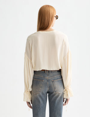 Person wearing a white blouse and blue jeans on a light gray background