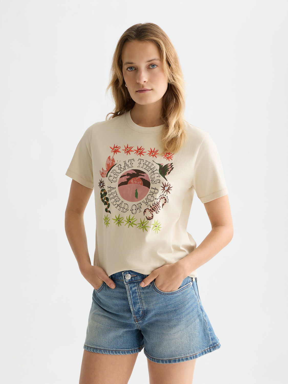 Woman wearing a graphic t-shirt and denim shorts on a plain background